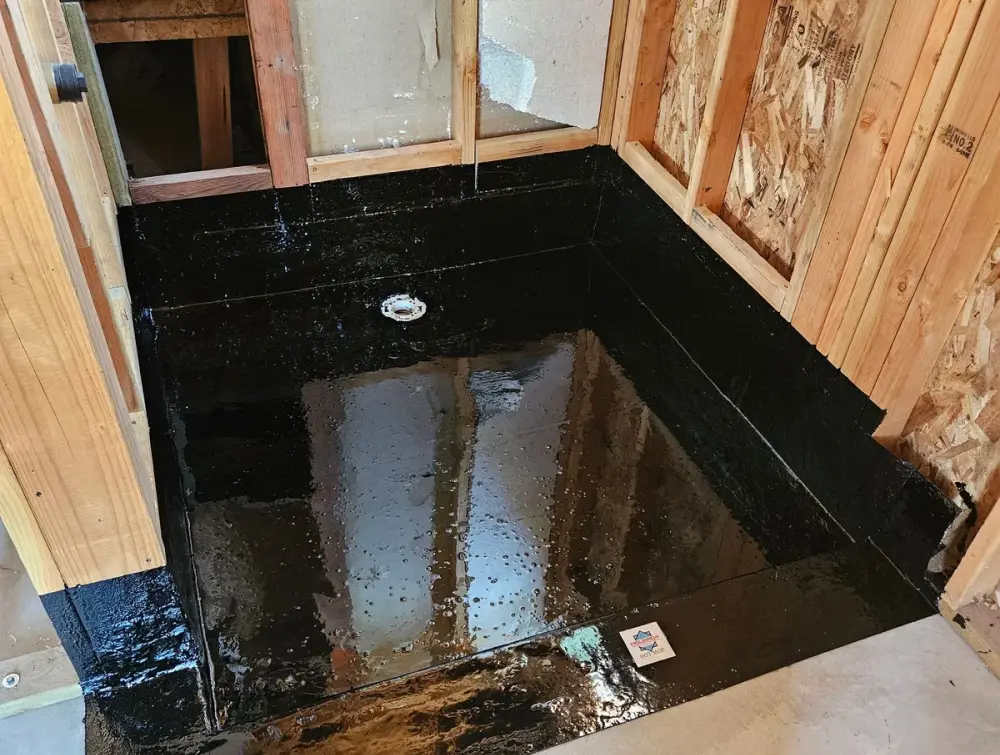 Un plato de ducha con hot mop terminado por Figueroa Shower Pans, con el agua todavía sobre la membrana negra, subida por las paredes y sobre el bordillo